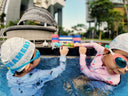 Two children in swim caps and goggles playing in a pool with a modern building in the background - Learn to Swim for Toddlers & Children in Singapore - Private Condo Swim Coaching