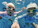 Two children wearing swim caps and goggles underwater in a pool - Condo Swimming Lesson for Children Singapore