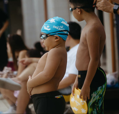 Two young boys in swim attire standing in a poolside waiting for their turn for swim meet