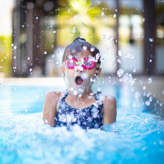 Child splashing confidently in an outdoor pool during a Dreamers swim lesson