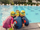 Three children wearing swim caps and goggles sitting by a pool - Swim Coach Talking to Students at the poolside - Swimming Lessons for Total Beginner Singapore