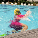 Child swimming in a pool wearing a yellow swim cap and pink swimsuit - Learn to Swim Toddlers - Condo Swimming Lessons personalised for young children Singapore