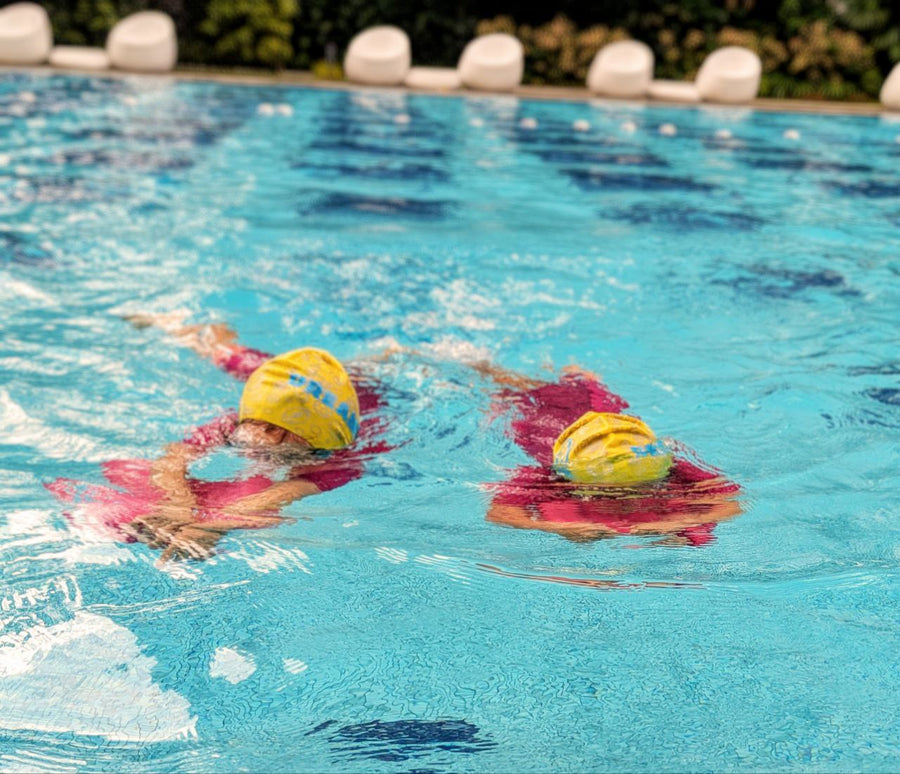 Two children with swim caps and kickboard in condominium pool Singapore
